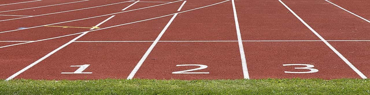 El inicio de las tres primeras pistas de carreras en un hipódromo, con suelo rojo y los números en blanco.