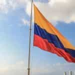 Bandera de Colombia ondeando en mástil sobre cielo con nubes.