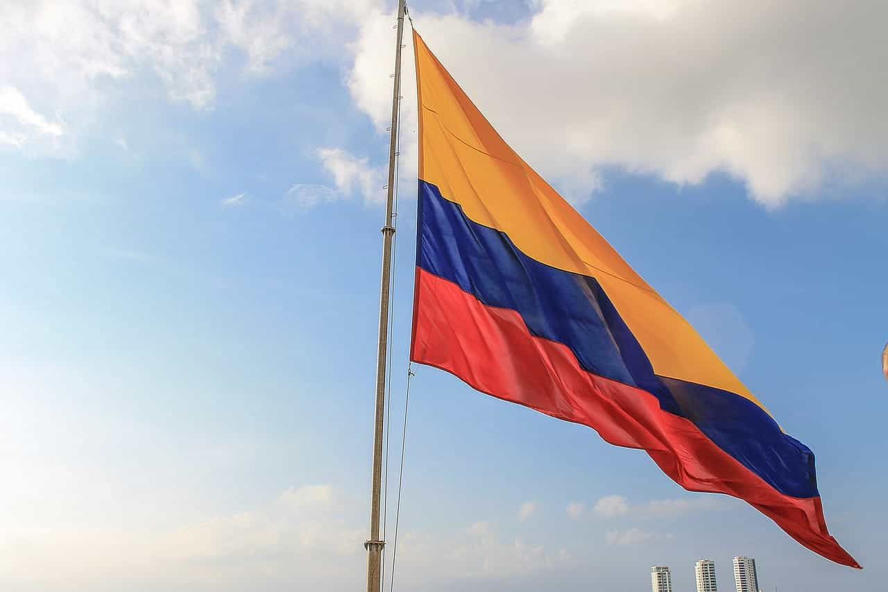 Bandera de Colombia ondeando en mástil sobre cielo con nubes.