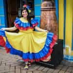 Mujer colombiana sonriendo, vestida con traje típico con los colores de la bandera.