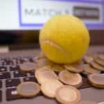 Pelota de tenis sobre ordenador portátil con pila de monedas.