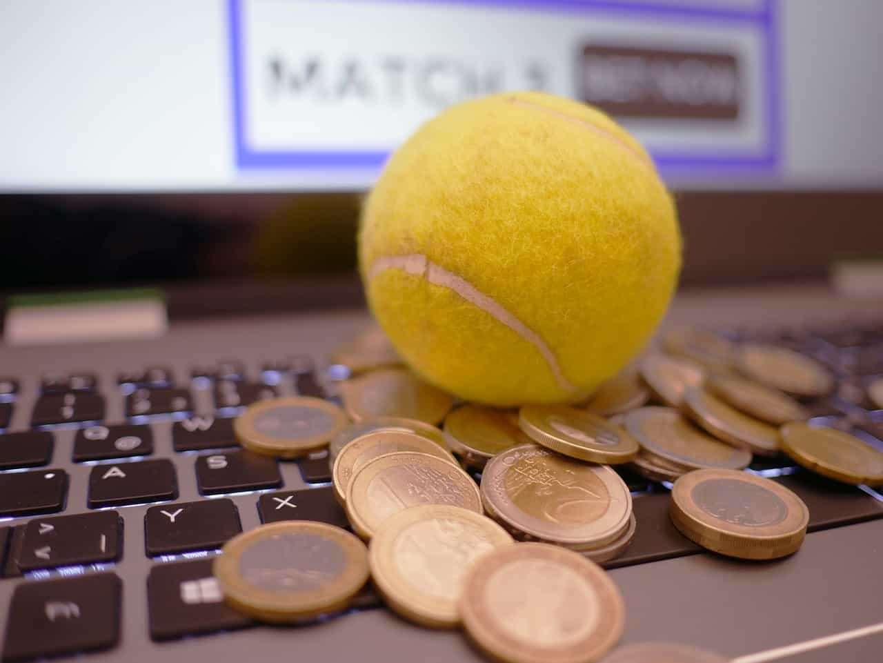 Pelota de tenis sobre ordenador portátil con pila de monedas.