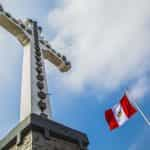 Bandera de Perú ondeando desde mástil junto a enorme monumento con forma de cruz católica.