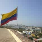 Bandera de Colombia ondeando sobre una cuesta con vista a una ciudad.