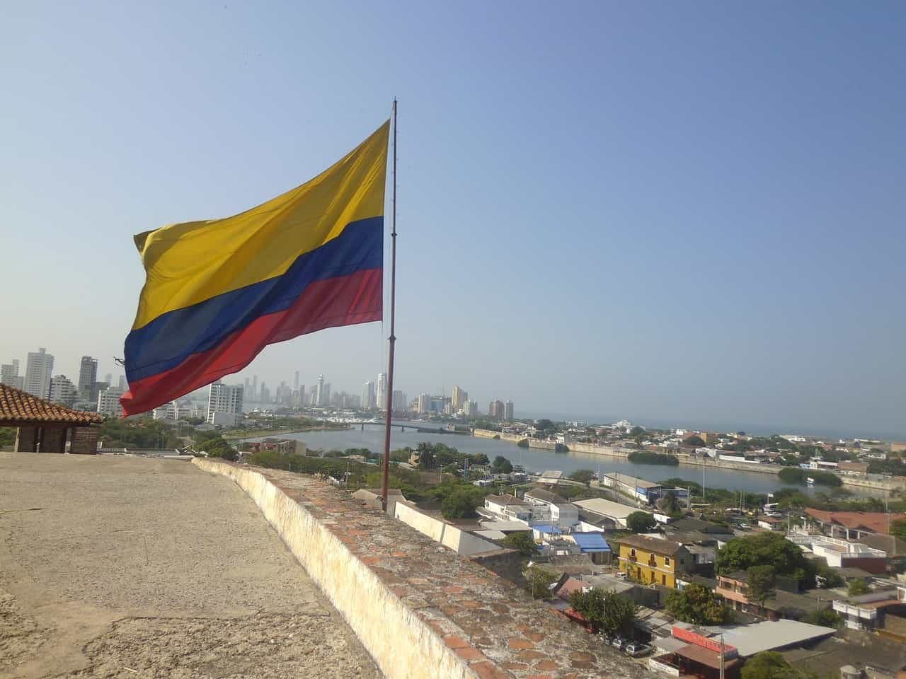 Bandera de Colombia ondeando sobre una cuesta con vista a una ciudad.